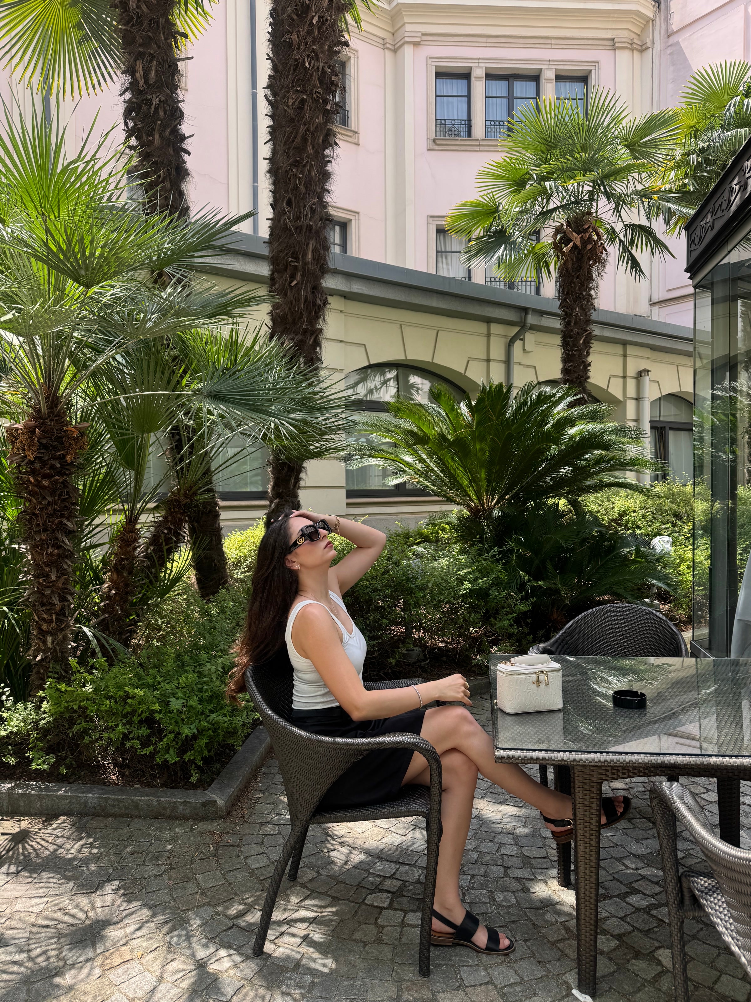 Tereza seated outdoors in a courtyard with palms.
