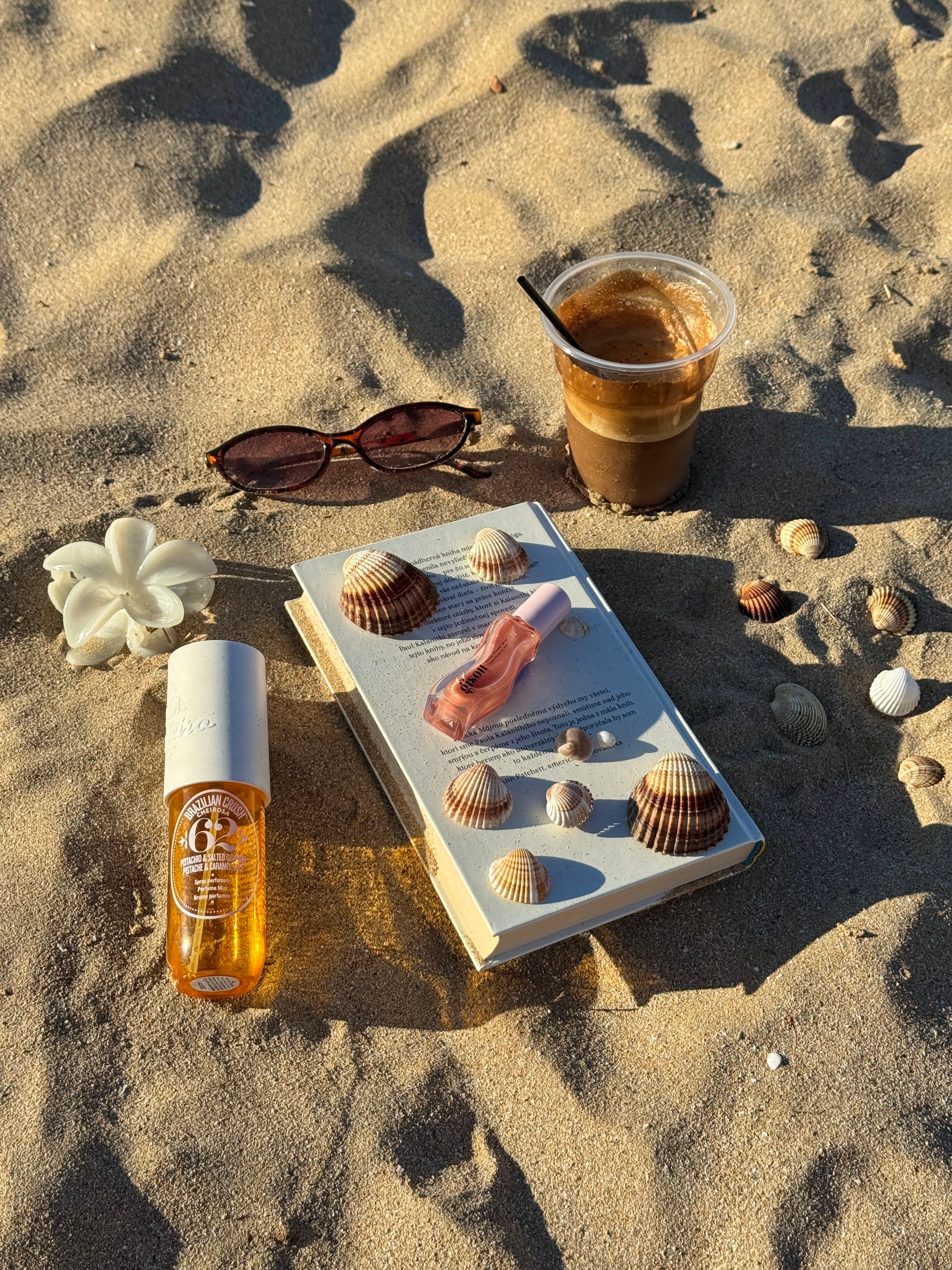 Beach still life with coffee, perfume, and book.