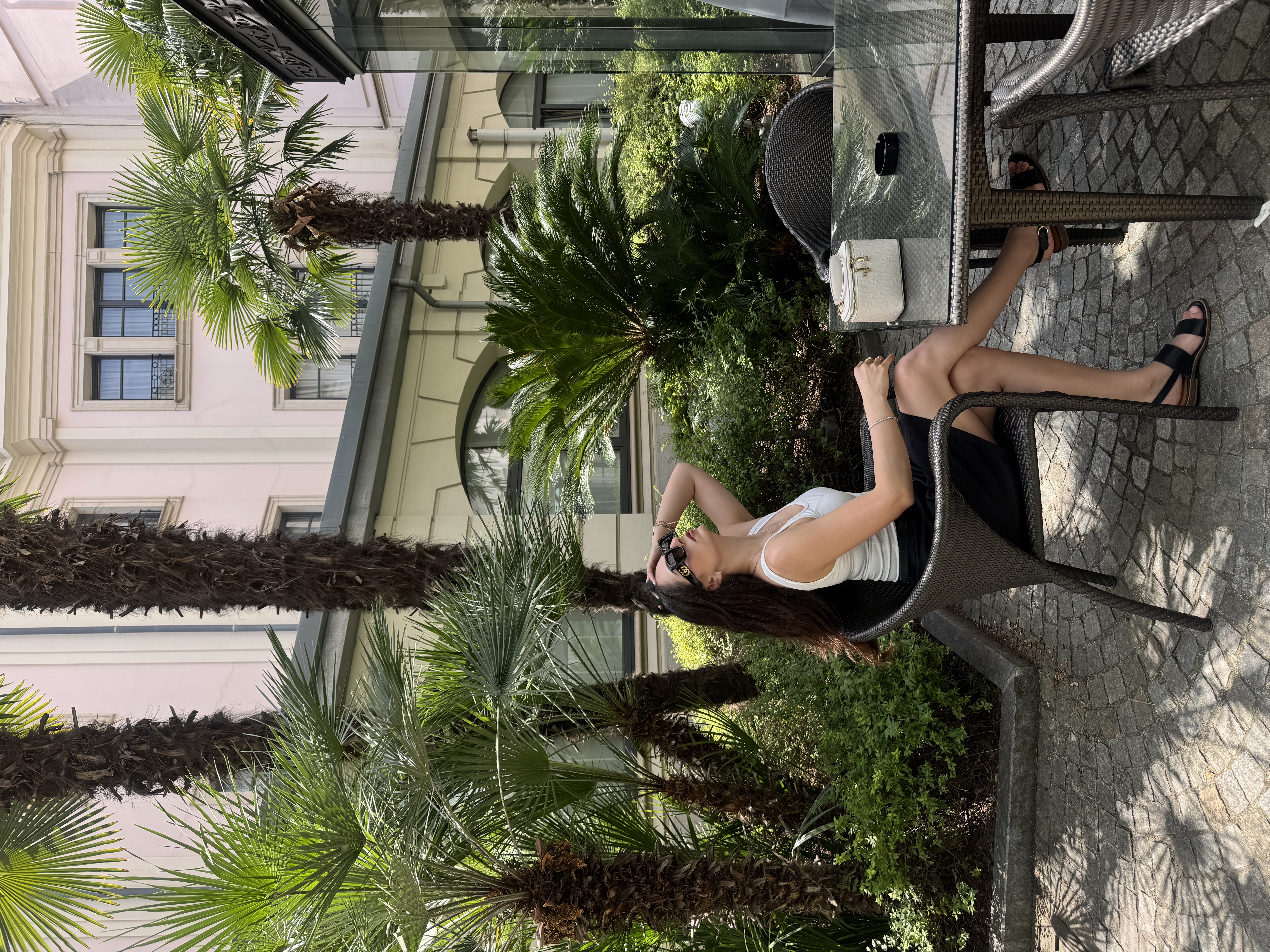 Tereza seated outdoors in a courtyard with palms.